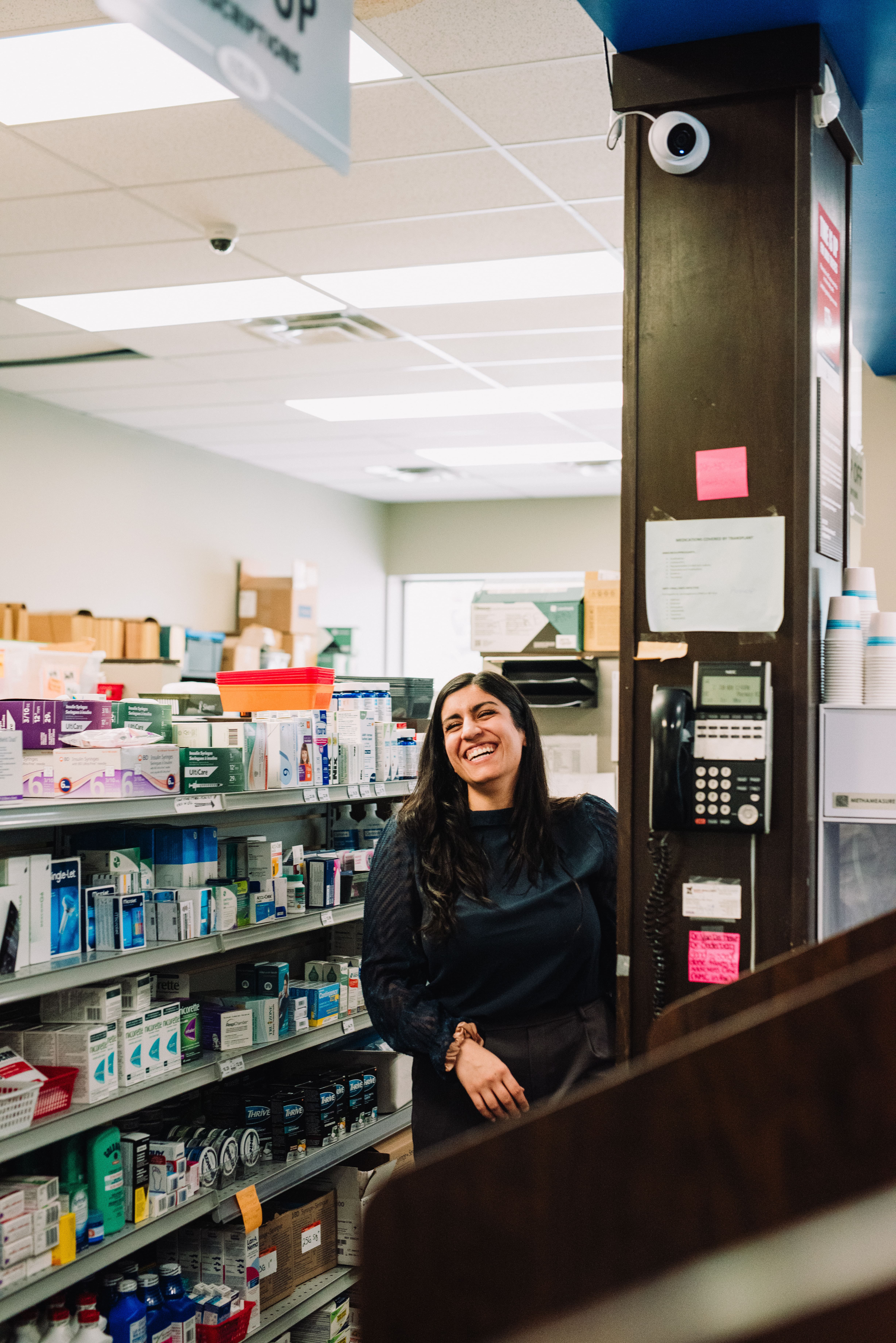 Kipp-Mallery Pharmacy team member smiling in dispensary area surrounded by medications and shelves in Kamloops