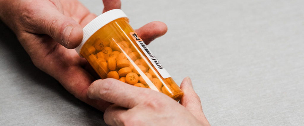 Hands holding an orange prescription pill bottle filled with medication at a local Kamloops pharmacy